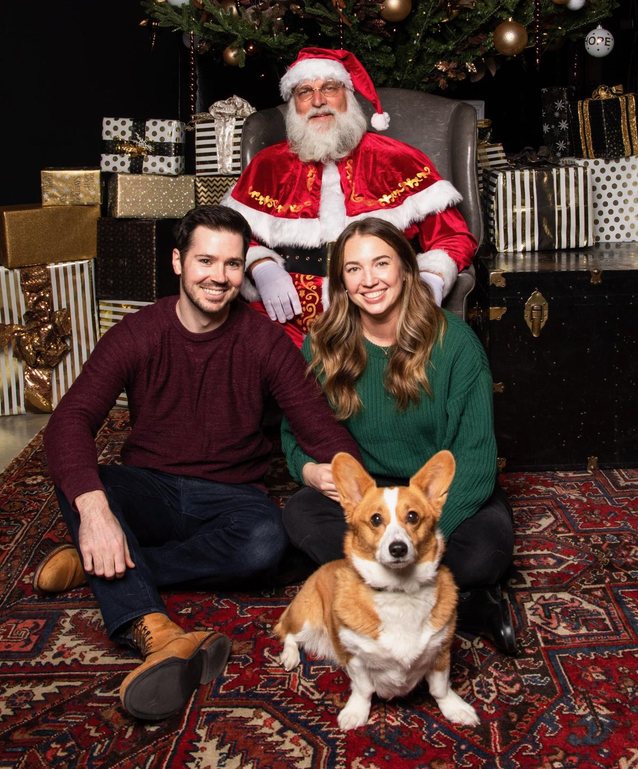 Jacob and Kim sitting on a rug with their corgi Phoebe, Santa behind them